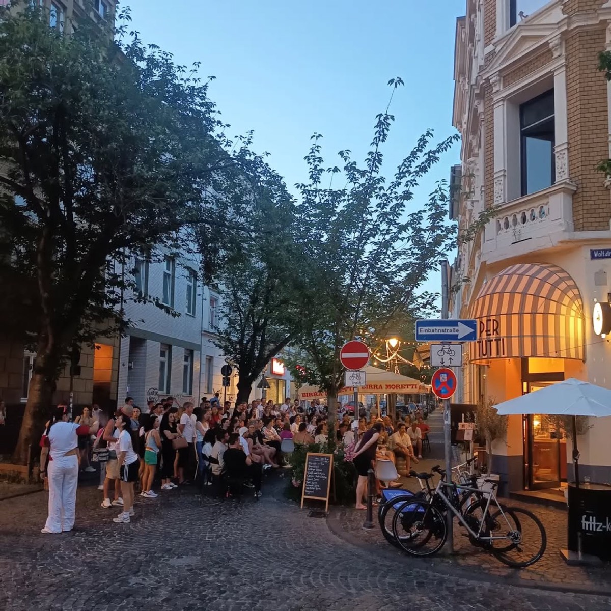 Abendstimmung: volle Straße vor dem Café Per Tutti